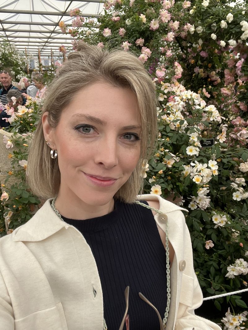 Sandy smiling in front of a cascade of pale pink and white climbing roses