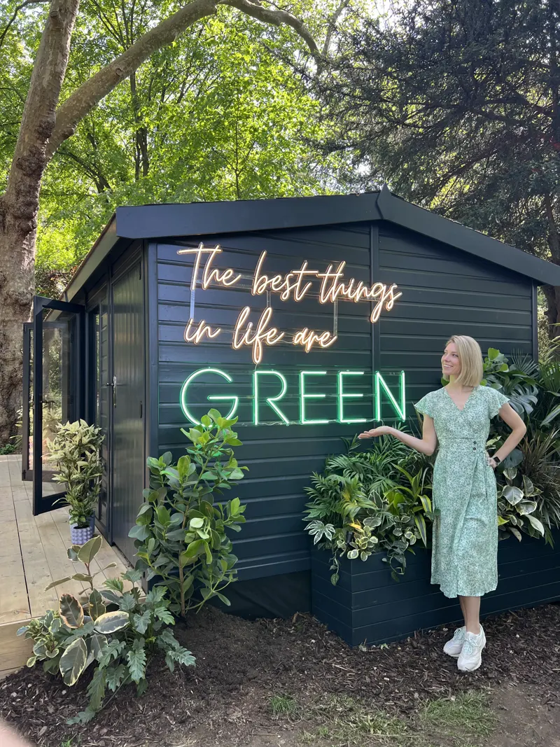Sandy beside a neon 'green' sign in a lush garden